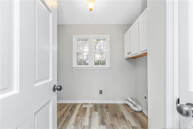 washroom with light hardwood / wood-style flooring, hookup for an electric dryer, cabinets, and a textured ceiling