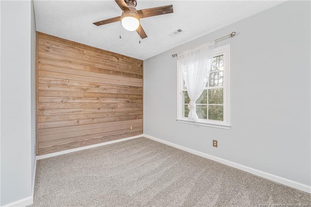 empty room with ceiling fan, wooden walls, and carpet floors