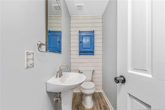 bathroom featuring a textured ceiling, wood walls, hardwood / wood-style flooring, and toilet