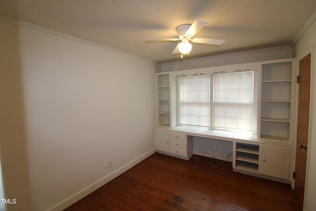 unfurnished office with crown molding, a textured ceiling, built in desk, dark hardwood / wood-style flooring, and ceiling fan