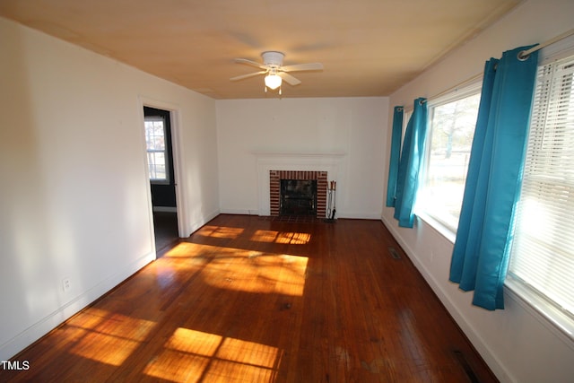 unfurnished living room featuring a brick fireplace, plenty of natural light, dark hardwood / wood-style floors, and ceiling fan