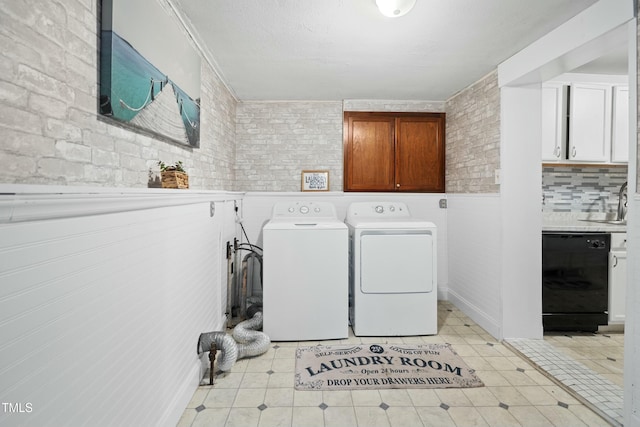 clothes washing area with sink, washer and dryer, and brick wall