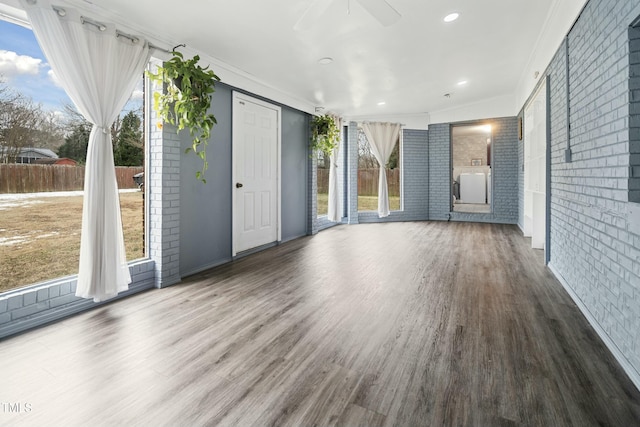 unfurnished living room featuring wood-type flooring, brick wall, ornamental molding, and ceiling fan