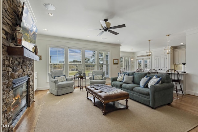 living room featuring crown molding, a stone fireplace, light hardwood / wood-style flooring, and ceiling fan