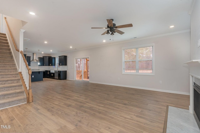 unfurnished living room with light wood-style flooring, a fireplace with flush hearth, baseboards, stairway, and crown molding