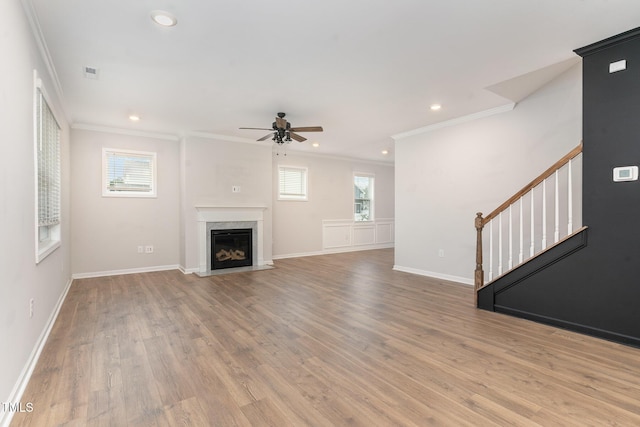 unfurnished living room with wood finished floors, visible vents, stairway, a glass covered fireplace, and crown molding