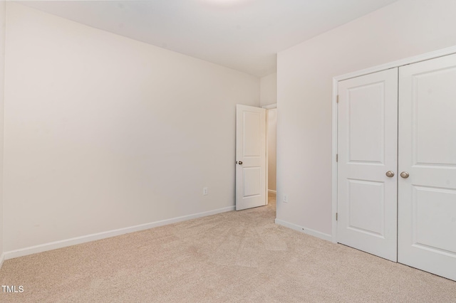 unfurnished bedroom featuring baseboards, a closet, and light colored carpet