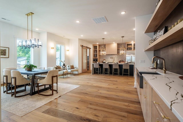 dining area with a notable chandelier, a barn door, and light wood-type flooring