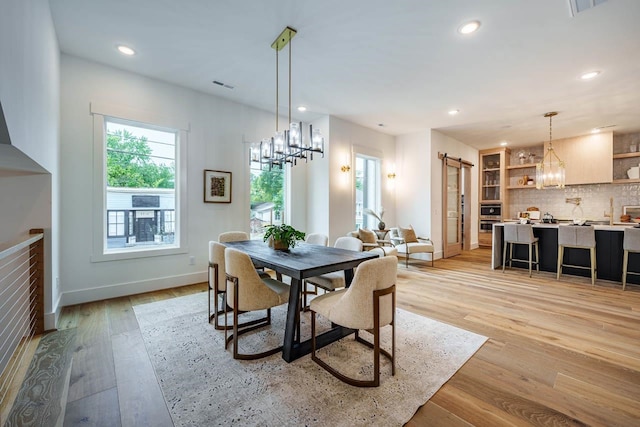 dining area featuring a barn door, an inviting chandelier, and light hardwood / wood-style flooring