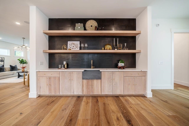 bar featuring a notable chandelier, sink, light hardwood / wood-style floors, and light brown cabinets