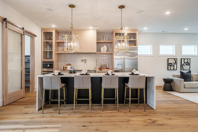 kitchen with a kitchen bar, stainless steel built in refrigerator, decorative light fixtures, a barn door, and light hardwood / wood-style floors