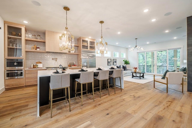 kitchen with pendant lighting, a spacious island, stainless steel appliances, and light hardwood / wood-style floors