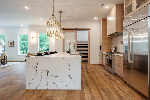 kitchen featuring high end appliances, hanging light fixtures, light hardwood / wood-style flooring, a barn door, and light stone countertops