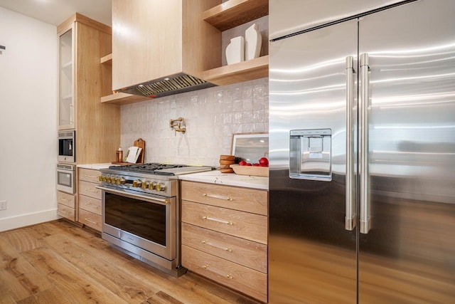 kitchen with tasteful backsplash, high end appliances, custom range hood, light brown cabinets, and light wood-type flooring