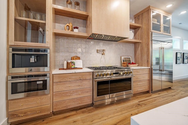 kitchen featuring light brown cabinetry, custom exhaust hood, tasteful backsplash, high quality appliances, and light hardwood / wood-style floors