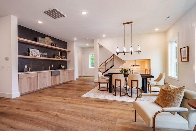 bar with pendant lighting, light brown cabinetry, light hardwood / wood-style flooring, and a notable chandelier