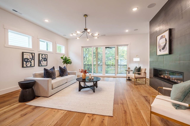 living room featuring an inviting chandelier, light hardwood / wood-style floors, and a tile fireplace