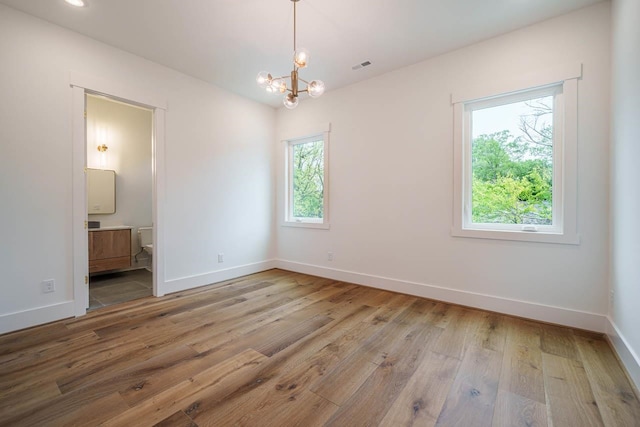 unfurnished room with plenty of natural light, a chandelier, and light wood-type flooring