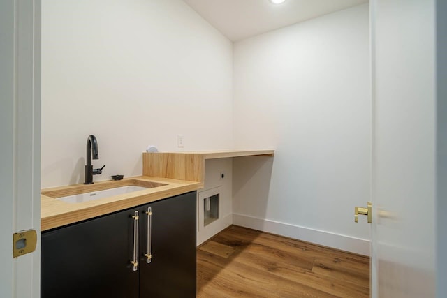 clothes washing area with electric dryer hookup, sink, cabinets, and light wood-type flooring