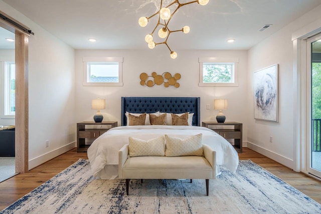 bedroom featuring a barn door, access to exterior, multiple windows, and light hardwood / wood-style flooring