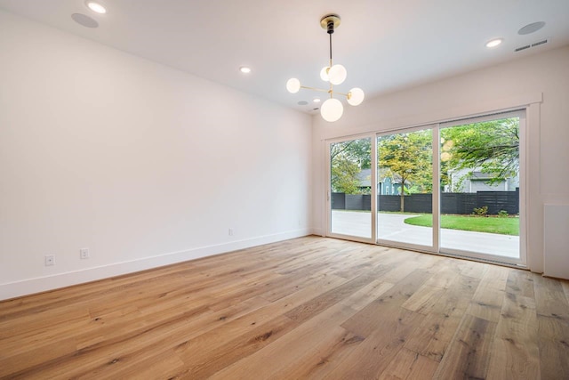 empty room featuring an inviting chandelier and light hardwood / wood-style flooring