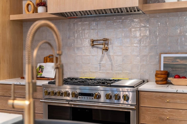 kitchen featuring light stone counters, decorative backsplash, wall chimney exhaust hood, and range with two ovens