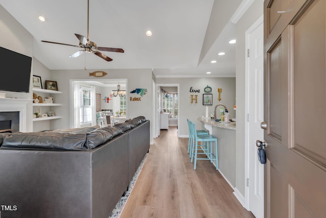 living room with crown molding, ceiling fan, sink, and light hardwood / wood-style floors