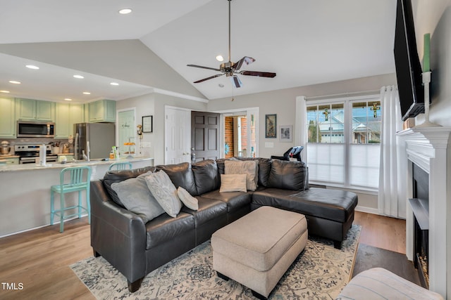 living room with lofted ceiling, ceiling fan, and light hardwood / wood-style flooring