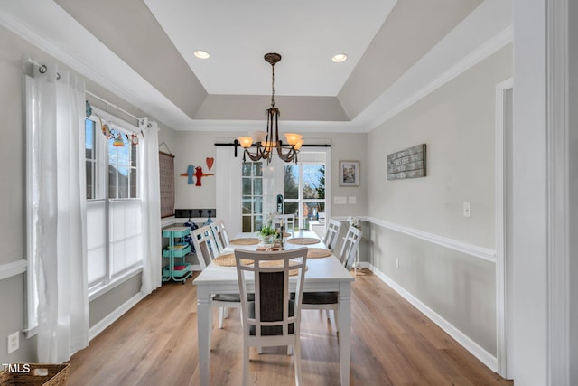 dining space with hardwood / wood-style flooring, ornamental molding, a notable chandelier, and a tray ceiling