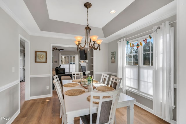 dining room featuring ornamental molding, ceiling fan with notable chandelier, hardwood / wood-style floors, and a tray ceiling