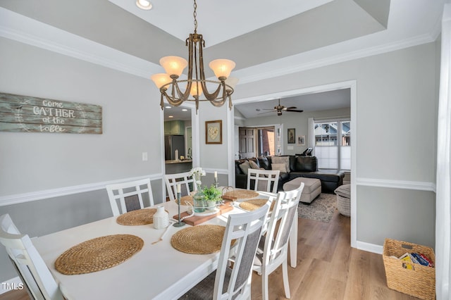 dining space featuring crown molding, a tray ceiling, light hardwood / wood-style flooring, and ceiling fan with notable chandelier