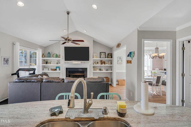 kitchen with sink, light stone counters, ornamental molding, ceiling fan with notable chandelier, and vaulted ceiling