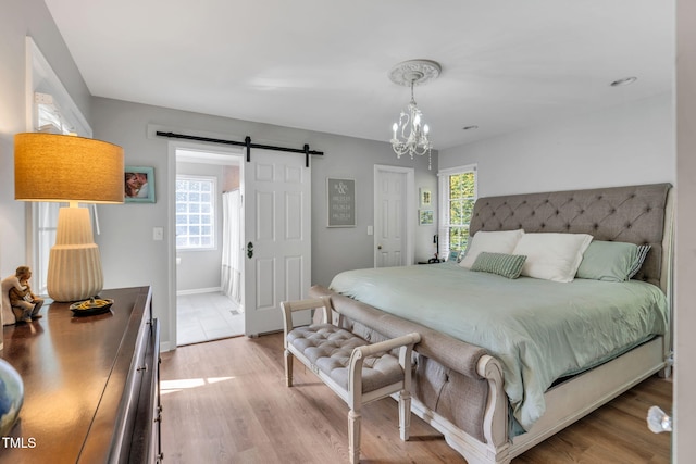 bedroom featuring an inviting chandelier, light hardwood / wood-style flooring, and a barn door