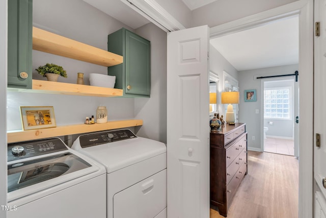 clothes washing area with light wood-type flooring, cabinets, washing machine and clothes dryer, and a barn door