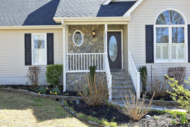 entrance to property with stone siding, covered porch, and a shingled roof