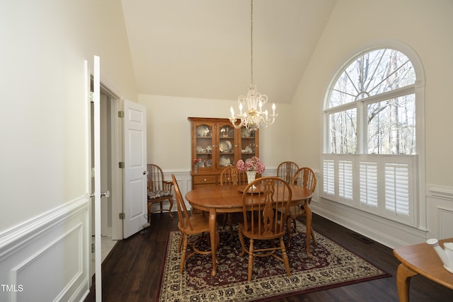 dining space with a notable chandelier, dark wood-type flooring, wainscoting, a decorative wall, and lofted ceiling