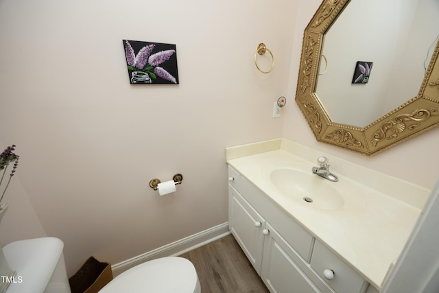 half bathroom with vanity, toilet, wood finished floors, and baseboards