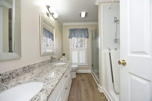 full bath featuring wood finished floors, a stall shower, a sink, crown molding, and toilet