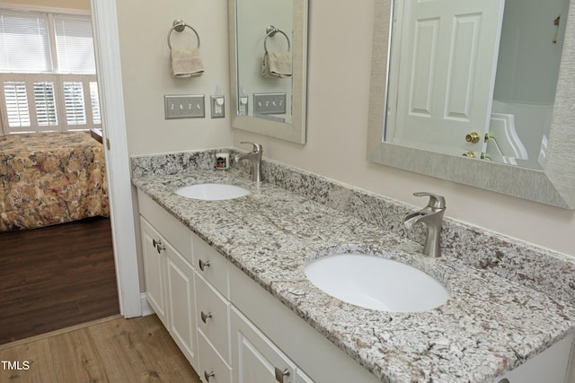 ensuite bathroom featuring a sink, connected bathroom, wood finished floors, and double vanity