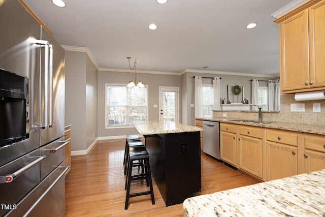 kitchen with stainless steel appliances, a breakfast bar, a center island, light stone countertops, and sink