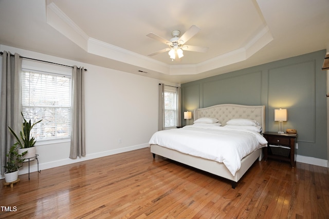 bedroom with ornamental molding, hardwood / wood-style flooring, ceiling fan, and a raised ceiling