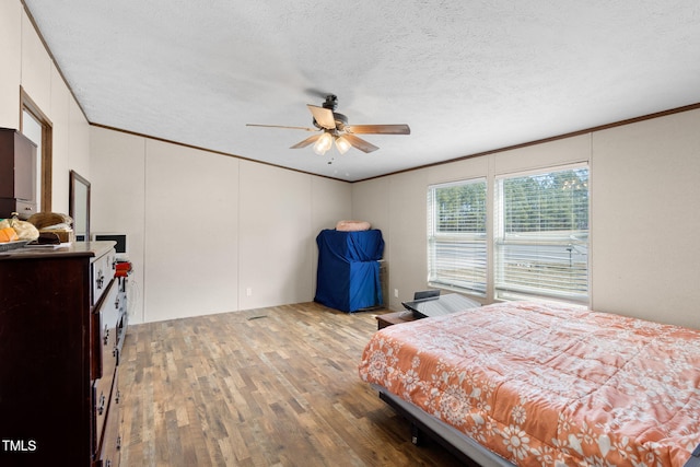 bedroom with a textured ceiling, wood finished floors, a ceiling fan, and crown molding