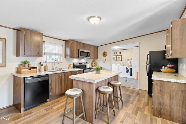 kitchen with light countertops, light wood-style floors, a sink, separate washer and dryer, and black appliances