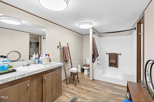 bathroom featuring shower / bathtub combination, toilet, ornamental molding, vanity, and wood finished floors