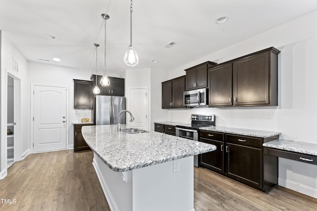 kitchen with sink, appliances with stainless steel finishes, a kitchen island with sink, light hardwood / wood-style floors, and backsplash