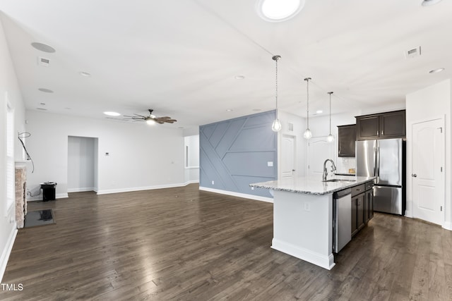 kitchen with appliances with stainless steel finishes, pendant lighting, an island with sink, sink, and light stone counters