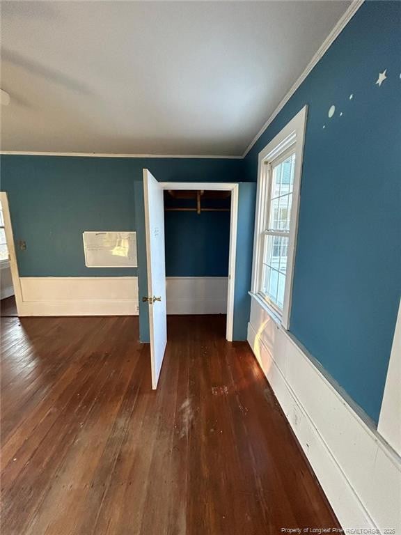 unfurnished bedroom featuring dark wood-type flooring, ornamental molding, and a closet