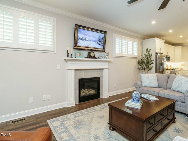 living room with a tiled fireplace, ornamental molding, dark hardwood / wood-style floors, and ceiling fan