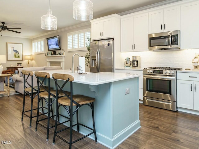 kitchen with appliances with stainless steel finishes, a breakfast bar, decorative light fixtures, white cabinets, and a center island with sink