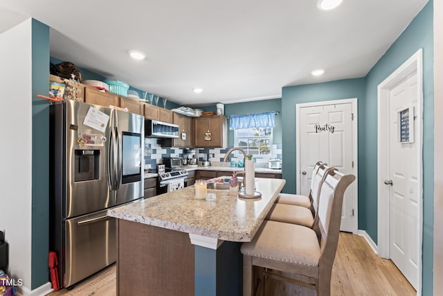 kitchen featuring sink, tasteful backsplash, a center island, appliances with stainless steel finishes, and light hardwood / wood-style floors